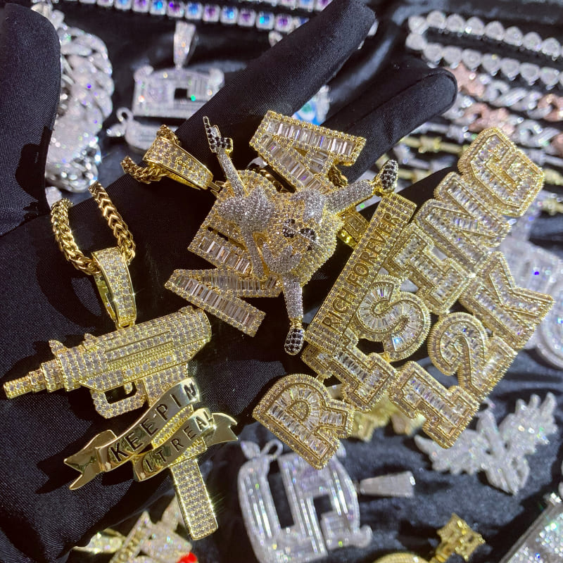 ICETOPLUXE iced out gun pendant displayed with other hip hop jewelry, perfect for making a statement